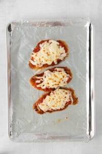 three chicken fingers on a baking sheet with cheese on top.