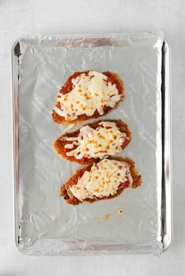 three chicken fingers on a baking sheet with cheese on top.