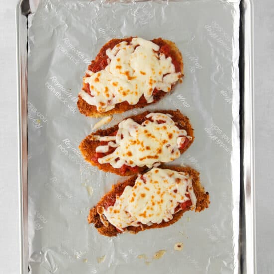 three chicken fingers on a baking sheet with cheese on top.