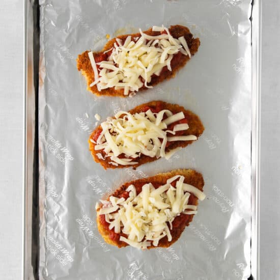 three chicken breasts topped with cheese on a baking sheet.