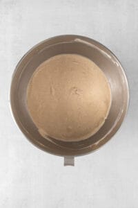a metal bowl filled with brown batter on a white surface.