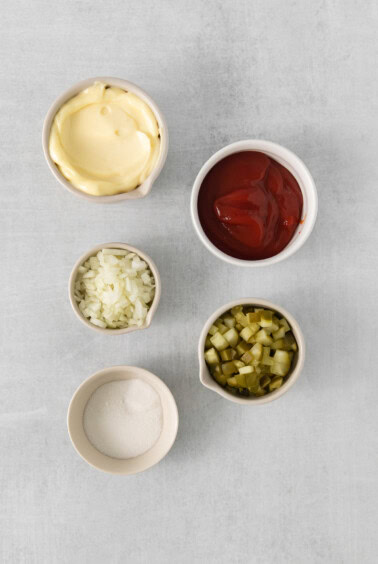 four bowls of ketchup, mustard, pickles and onions.