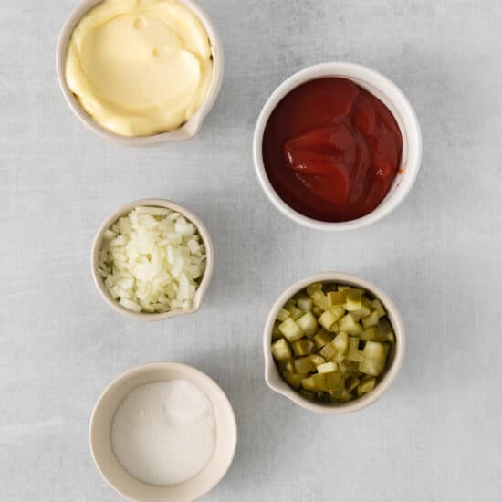 four bowls of ketchup, mustard, pickles and onions.
