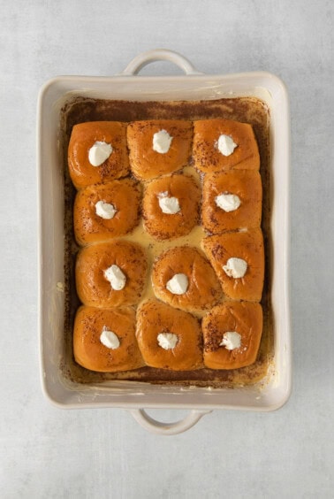 a baking dish filled with cinnamon rolls and whipped cream.