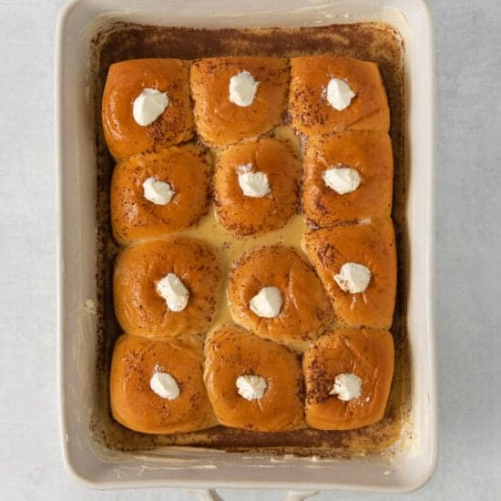 a baking dish filled with cinnamon rolls and whipped cream.