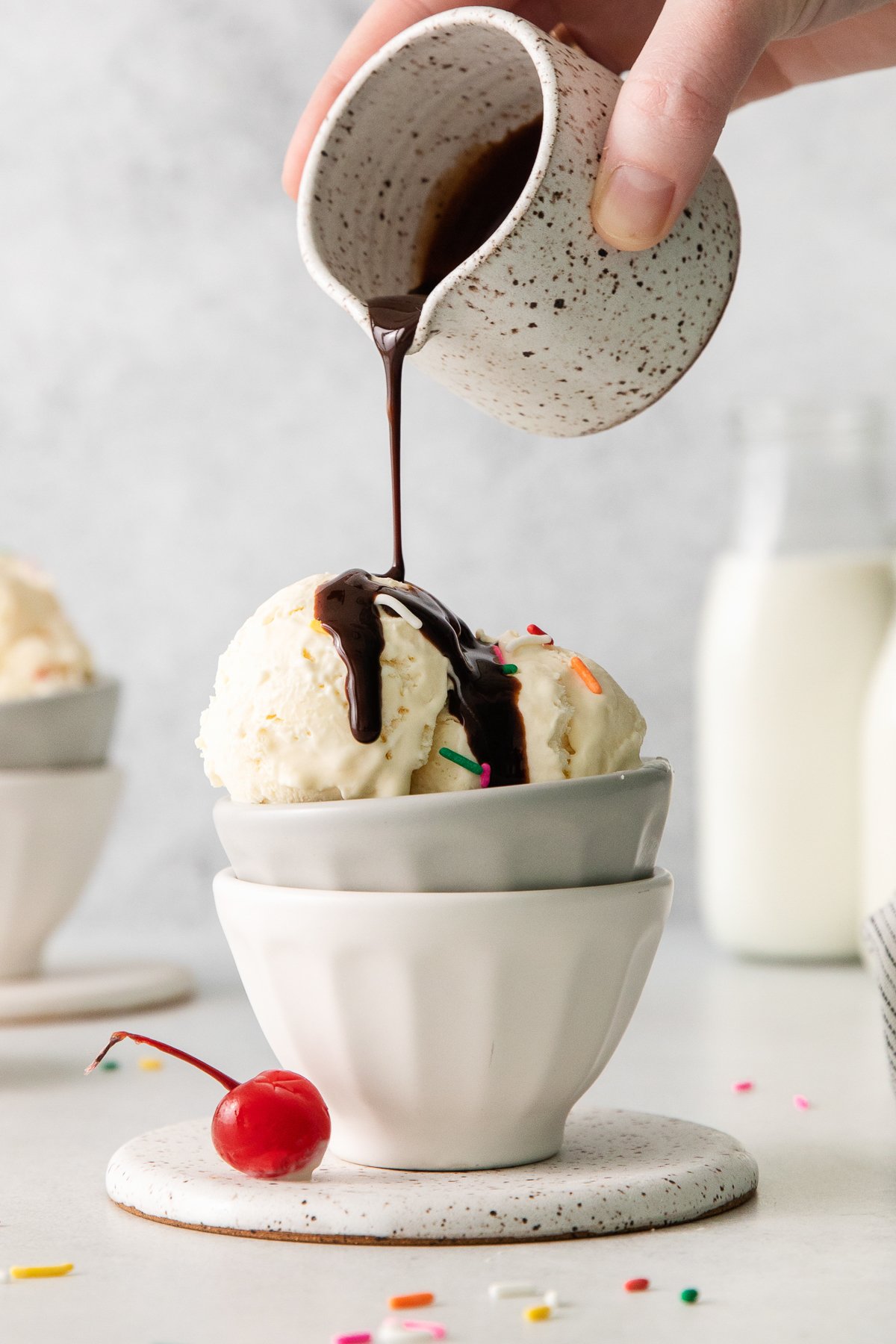 a person pouring ice cream into a bowl with a cherry on top.