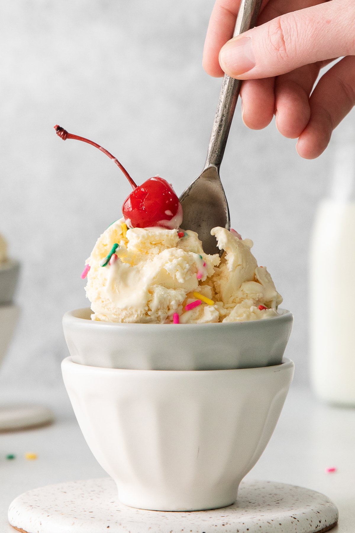 a person scooping ice cream into a bowl with a cherry on top.