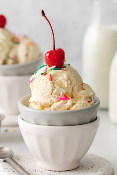 two bowls of ice cream with cherries and sprinkles.