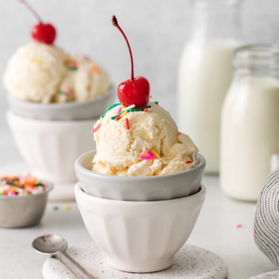 two bowls of ice cream with cherries and sprinkles.