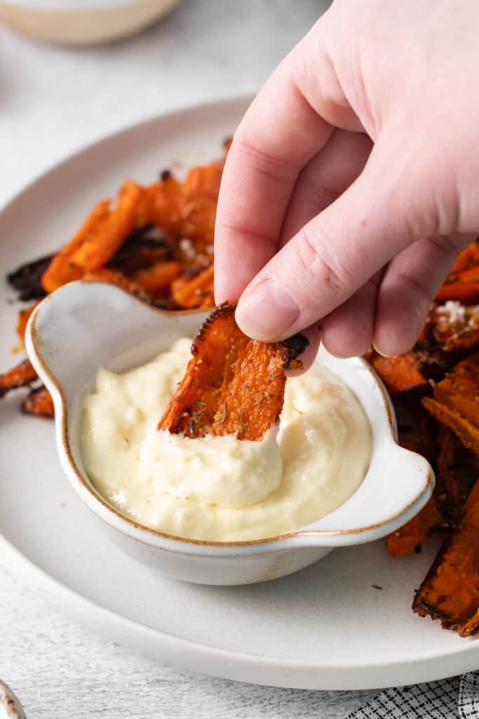 A hand dipping a parmesan smashed carrot in homemade aioli.