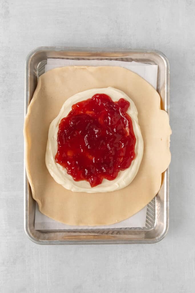 Cream cheese and strawberry jam spread on a pie crust.