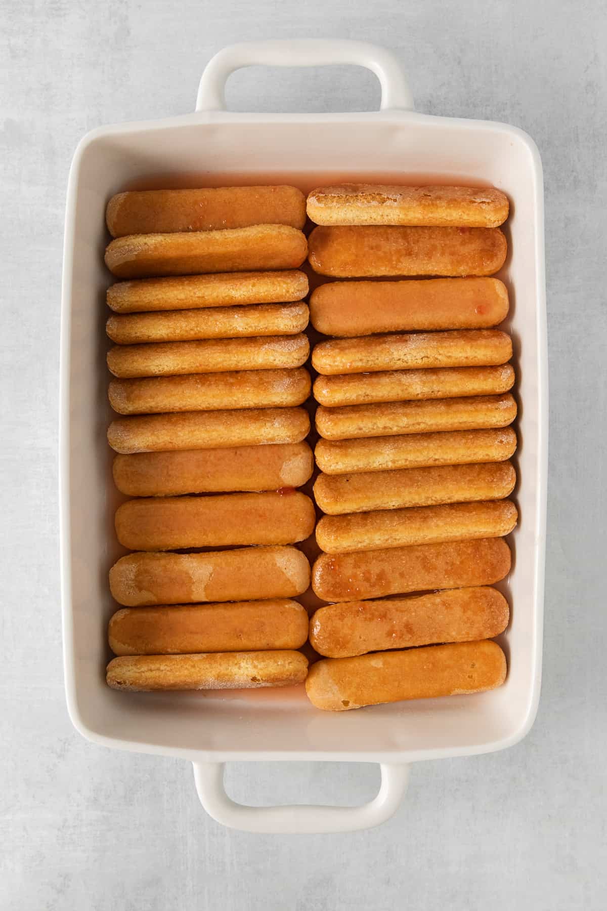 Lady fingers soaking in prosecco in a baking dish.