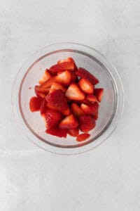 sliced strawberries in a glass bowl on a grey background.