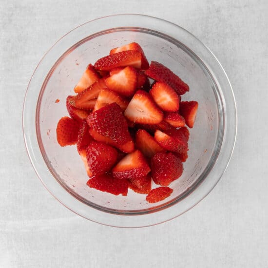 sliced strawberries in a glass bowl on a grey background.