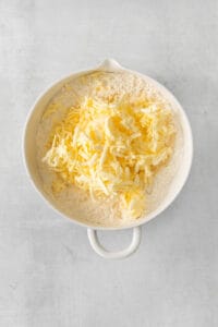 shredded cheese in a white bowl on a grey background.