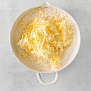 shredded cheese in a white bowl on a grey background.