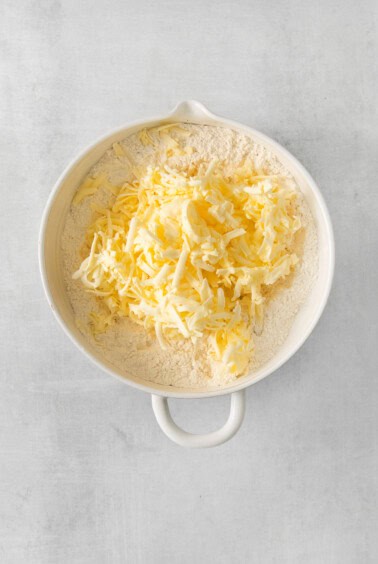 shredded cheese in a white bowl on a grey background.