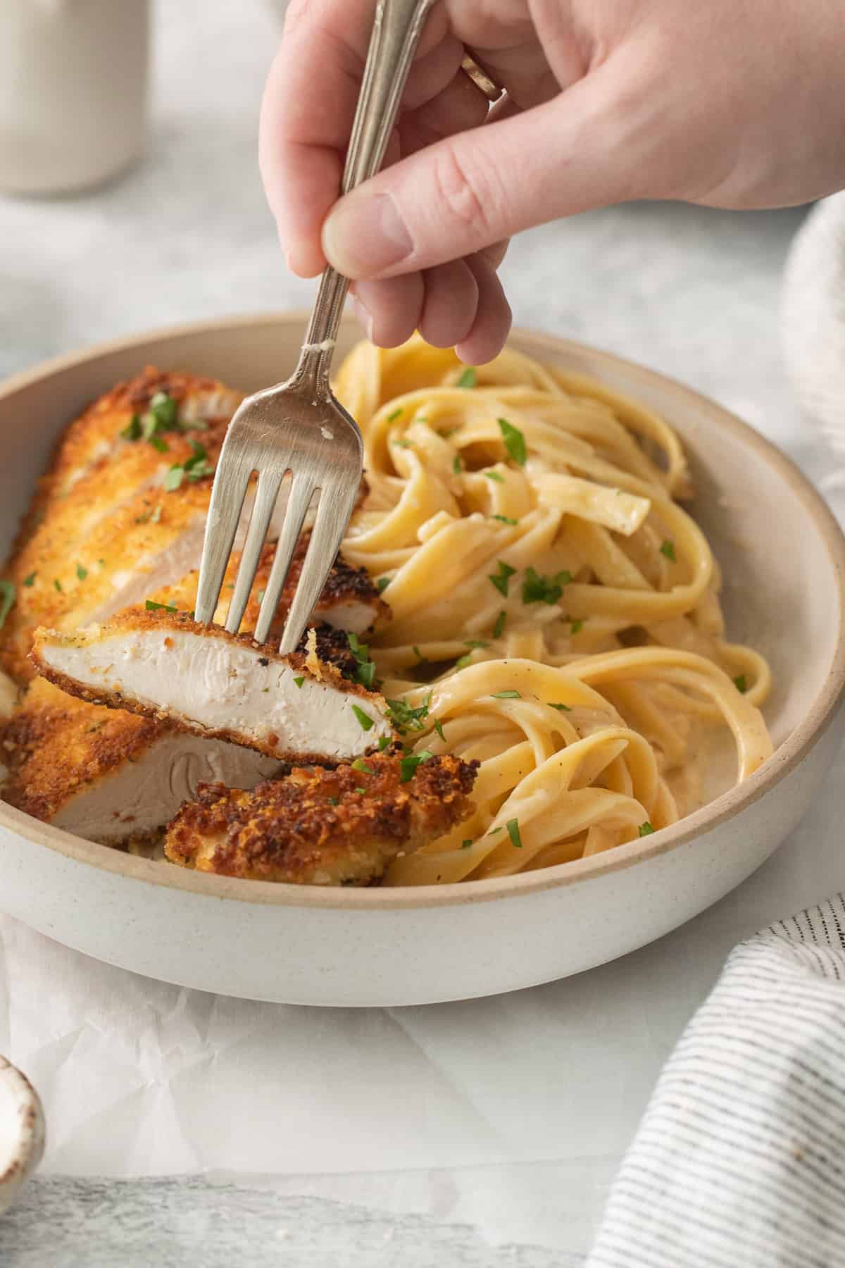 a person holding a fork over a plate of pasta and chicken.