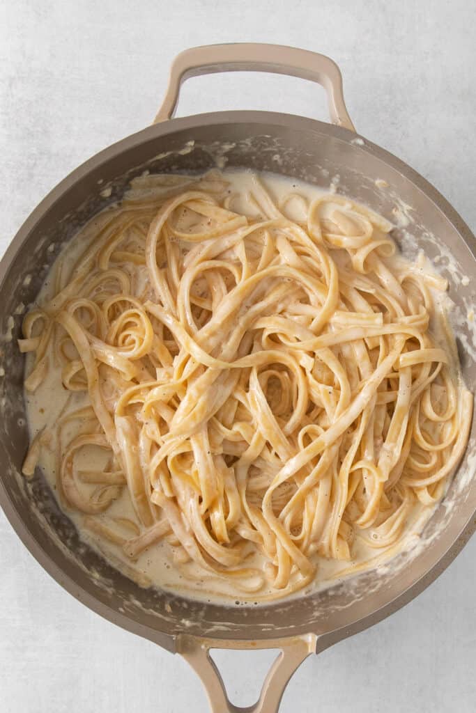 pasta tossed in alfredo sauce in a pan.