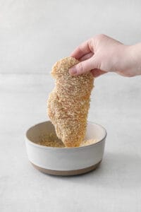a hand is holding a bowl of sesame seeds.