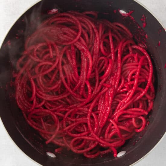 beet noodles being cooked in a pan.