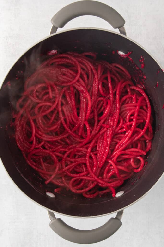 beet noodles being cooked in a pan.