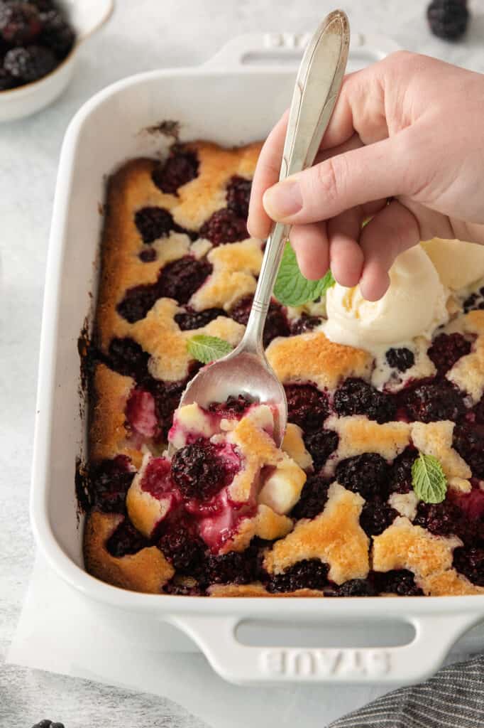 a person scooping ice cream onto a blueberry cobbler.