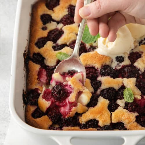 a person scooping ice cream onto a blueberry cobbler.