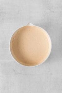 a bowl of orange sauce on a white surface.