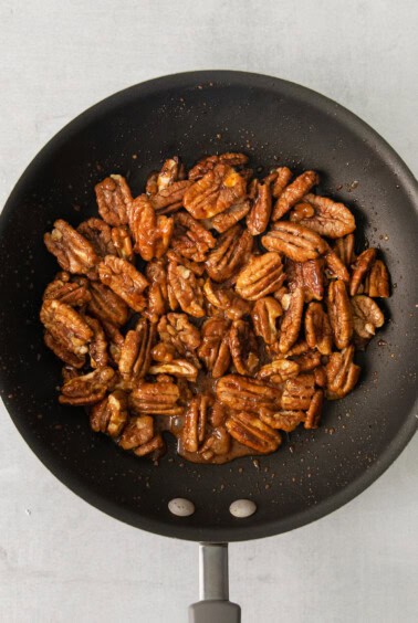pecans in a frying pan on a white background.