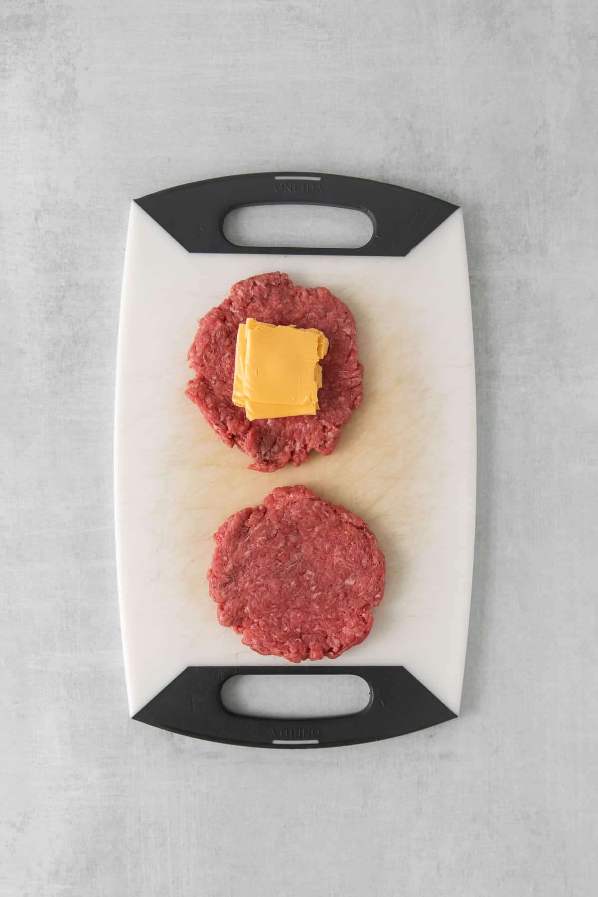 Raw beef patty with a square of american cheese on it.