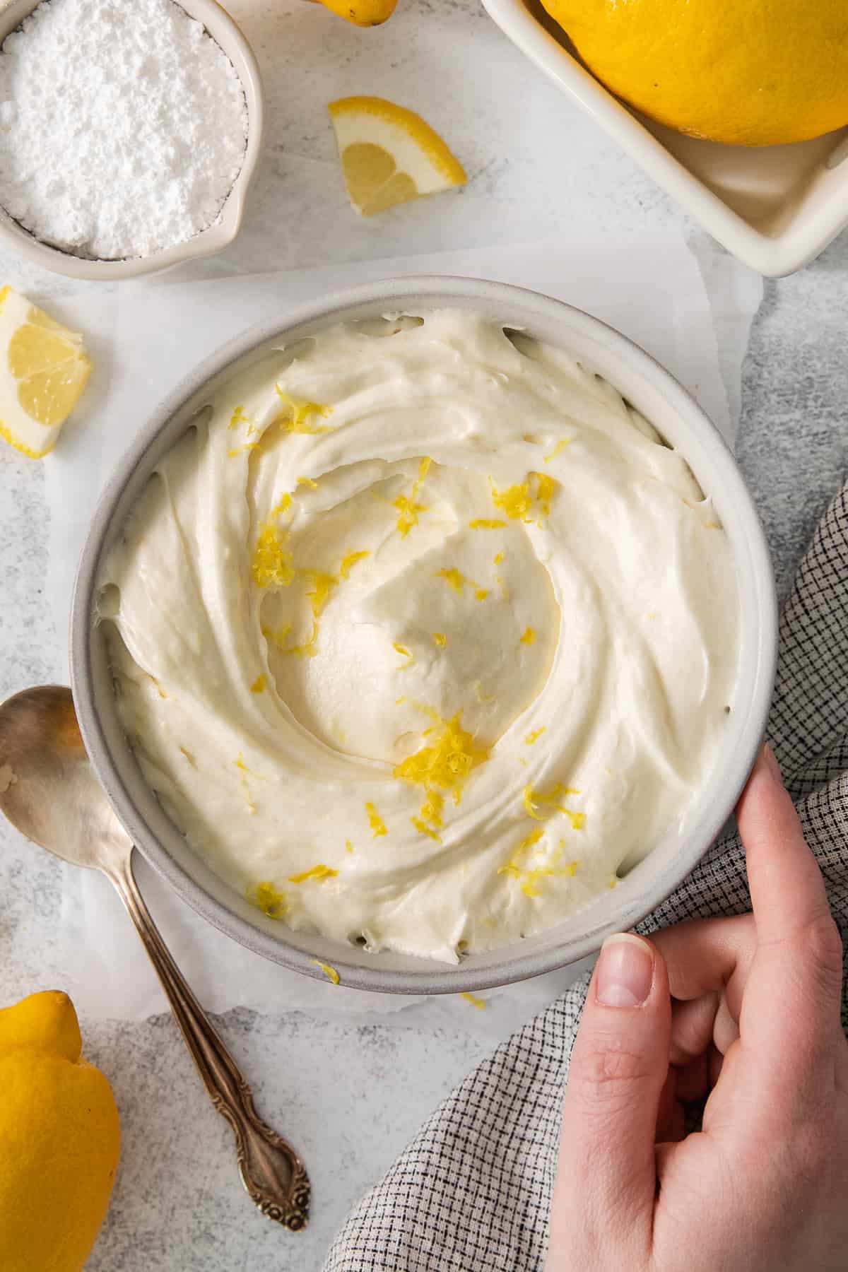 This lemon cream cheese frosting is the perfect compliment to your summertime desserts! The rich frosting gets balanced out with a delicious bright lemon flavor made from fresh lemons. Lemon cream cheese frosting in a bowl topped with lemon zest.
