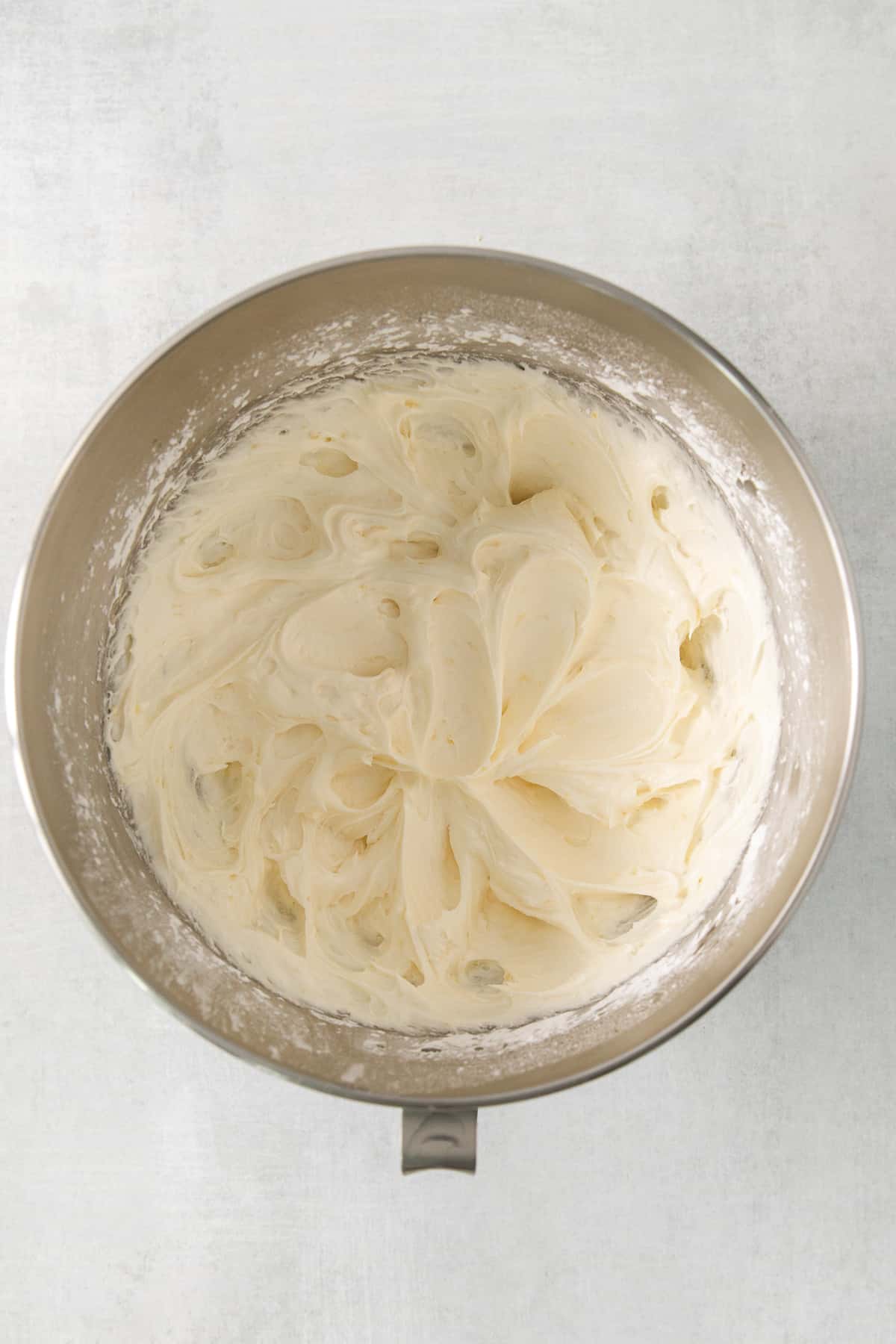 This lemon cream cheese frosting is the perfect compliment to your summertime desserts! The rich frosting gets balanced out with a delicious bright lemon flavor made from fresh lemons. Lemon cream cheese frosting whipped in a bowl.