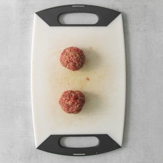 a cutting board with two meatballs on it.