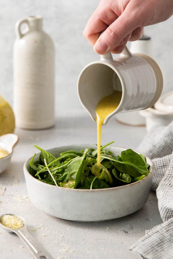 a person pouring dressing into a bowl of greens.