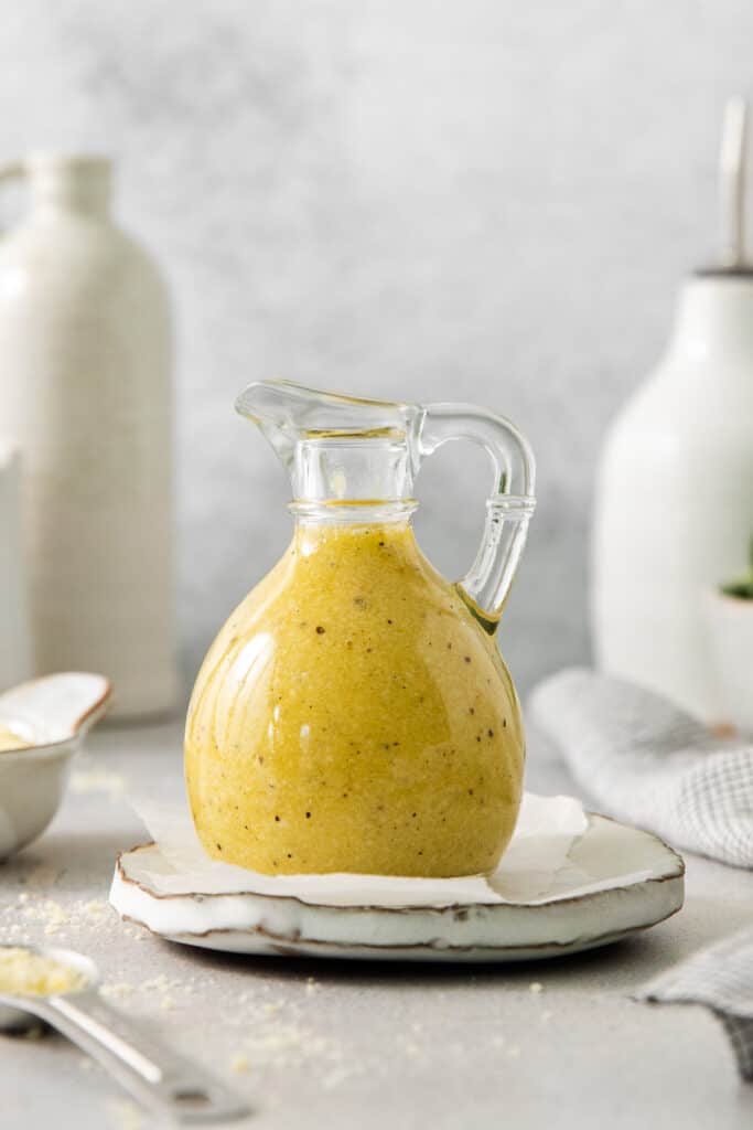 a glass jug of mustard sitting on top of a plate.