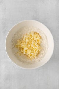 shredded cheese in a bowl on a white surface.