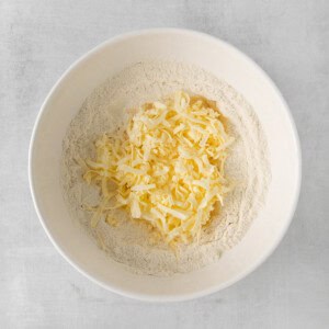 shredded cheese in a bowl on a white surface.