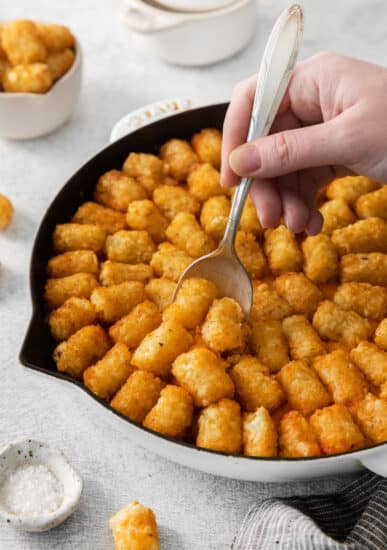 a person scooping tater tots out of a skillet.