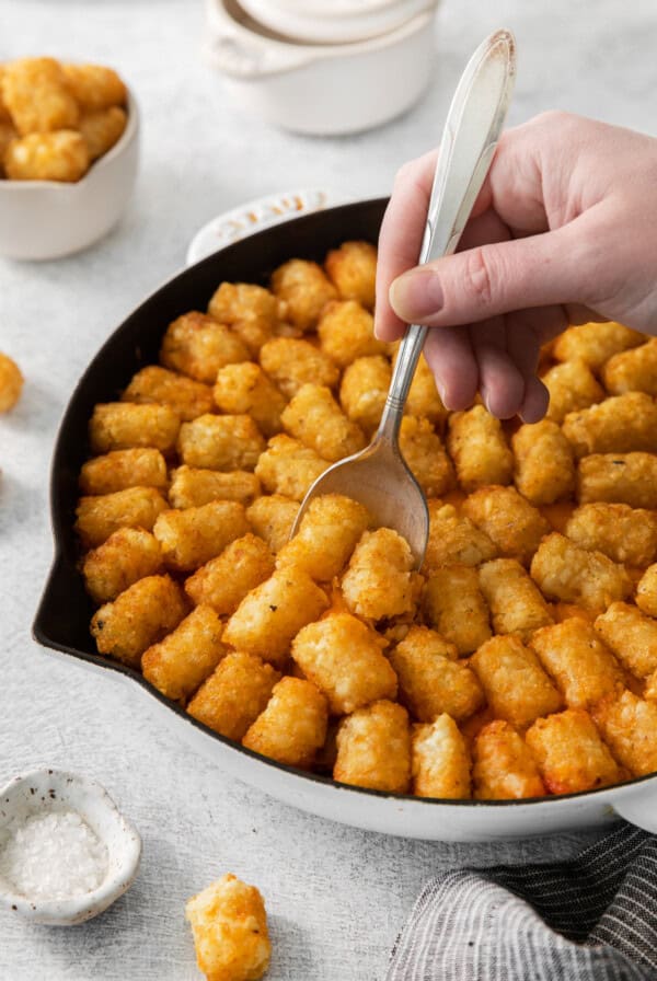 a person scooping tater tots out of a skillet.