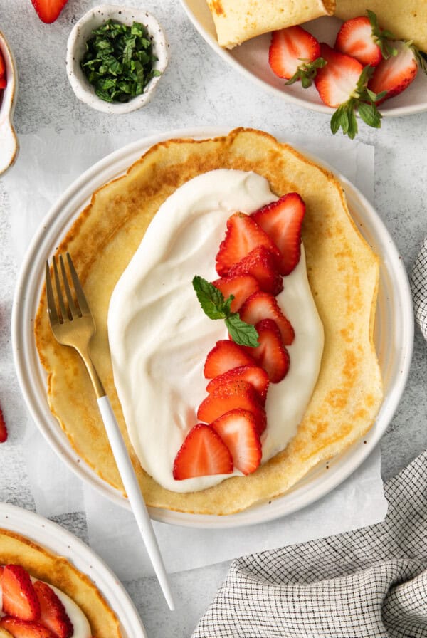 a plate of crepes with whipped cream and strawberries.