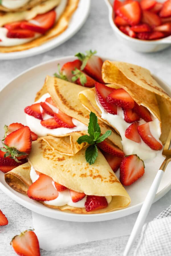 Strawberry crepes on a plate with a fork.