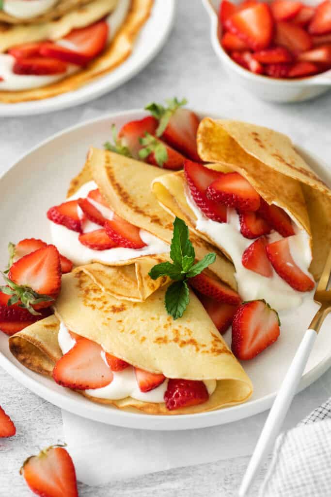 Strawberry crepes on a plate with a fork.