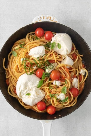 a skillet filled with spaghetti, tomatoes and mozzarella.
