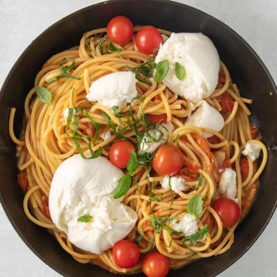 a skillet filled with spaghetti, tomatoes and mozzarella.