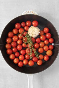 a frying pan filled with tomatoes and a sprig of thyme.