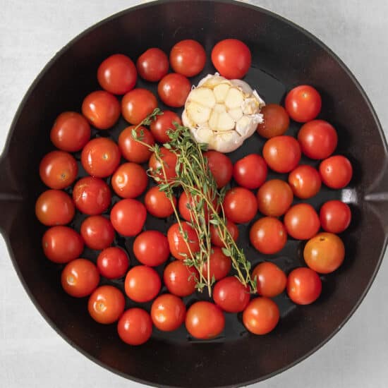 a frying pan filled with tomatoes and a sprig of thyme.