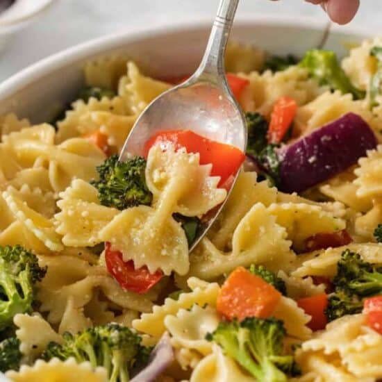 a spoonful of pasta with vegetables and broccoli in a white bowl.