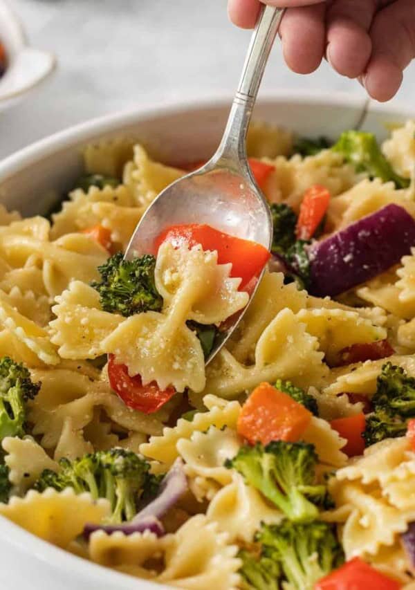 a spoonful of pasta with vegetables and broccoli in a white bowl.