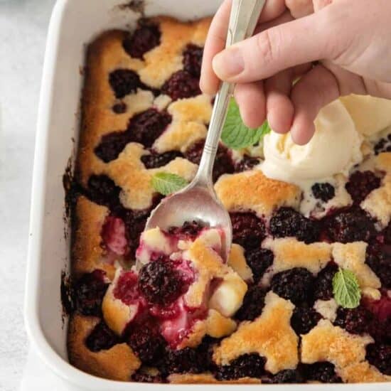 a person scooping blackberry cobbler from a baking dish.